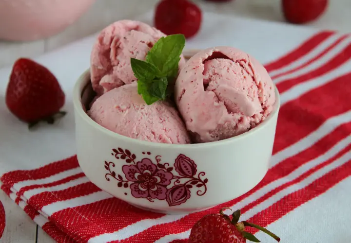 Pyszne lody truskawkowe w miseczce, ozdobione miętą. Idealne na lato, pokazują, jak zrobić lody truskawkowe.