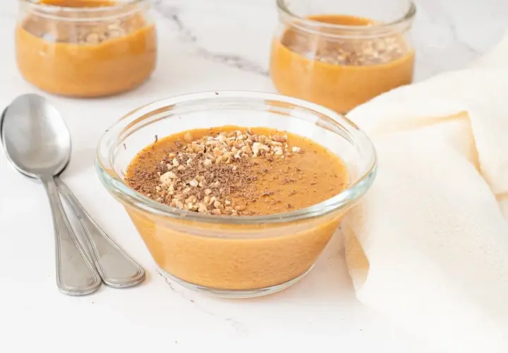 Delicioso postre cremoso, como baba de camelo, servido en un cuenco de cristal y espolvoreado con frutos secos y virutas de chocolate.