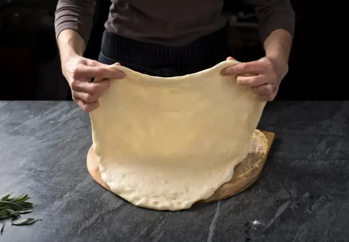 Ręce rozciągają elastyczne ciasto na pizzę, idealne do szybkiego przepisu na ciasto do pizzy.