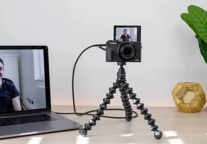 Configuración para usar webcam como cámara de seguridad: una Canon G7X en un trípode flexible, conectada a un portátil que muestra a un hombre sonriendo.