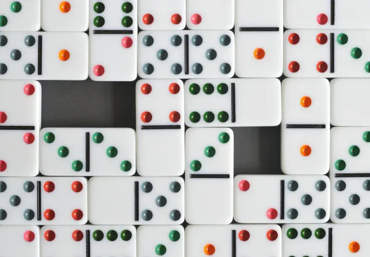 Wiele białych kostek do gry w domino z kolorowymi kropkami, ułożonych w rzędach. To klasyczna domino gra.