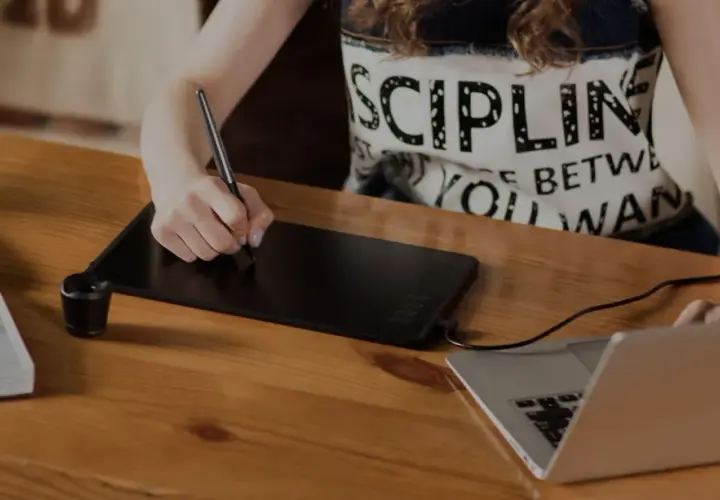 Osoba rysuje na tablecie graficznym, który służy do cyfrowego tworzenia grafiki i ilustracji, podłączonym do laptopa.