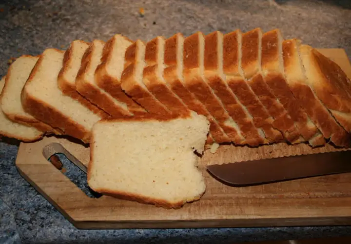 Tranches de pâte à pain de mie dorées et moelleuses, prêtes à être dégustées sur une planche en bois avec un couteau.