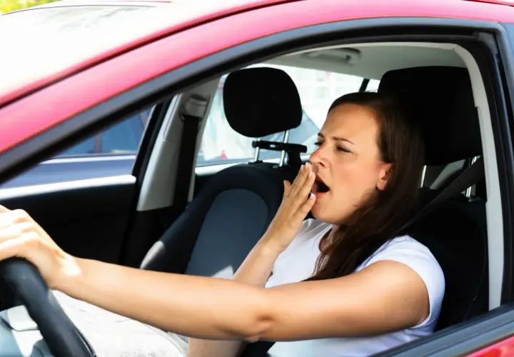 Mujer bosteza al volante, un claro ejemplo de qué puede causar somnolencia en un conductor.