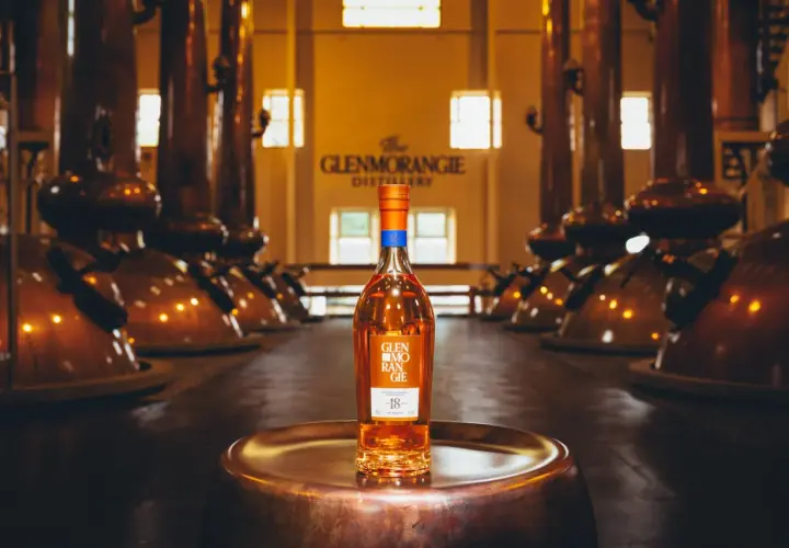 Bouteille de whisky Glenmorangie 18 ans posée sur un plateau en cuivre, au cœur de la distillerie Glenmorangie, entourée d'alambics en cuivre.