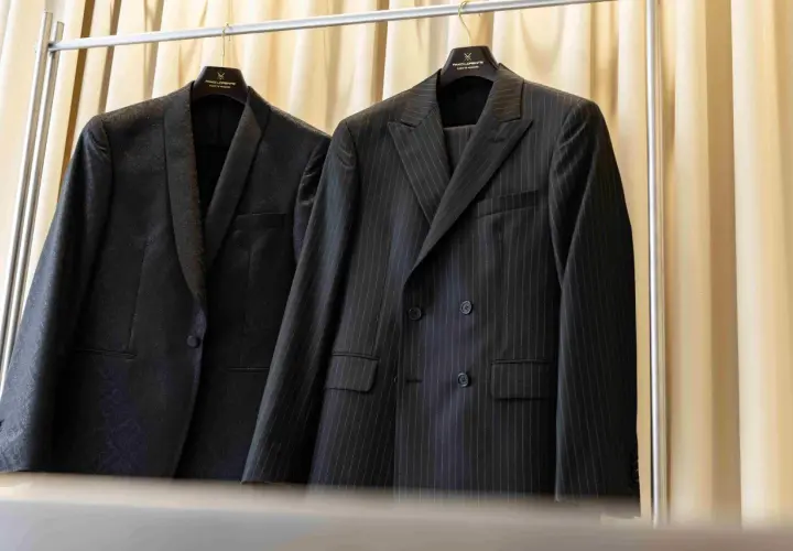 Dwa eleganckie garnitury wiszą na wieszakach. Jeden w prążki, drugi z subtelnym wzorem. Prasowanie garnituru to klucz do nienagannego wyglądu.