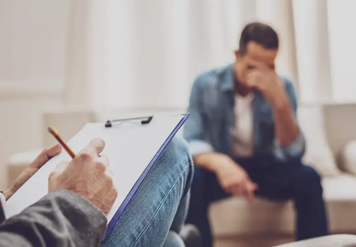 Rozmowa z terapeutą o trudnym rozwodzie z osobą chorą psychicznie. Mężczyzna w rozpaczy, terapeuta notuje.
