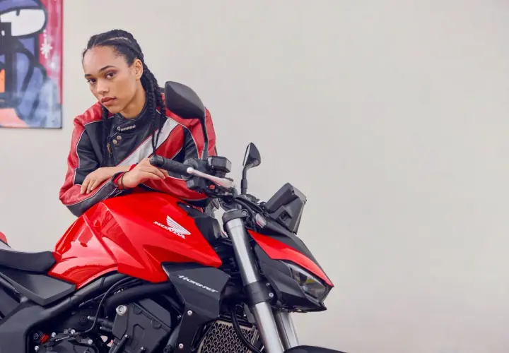 Joven con chaqueta de cuero posa junto a una moto roja Honda Hornet. Lista para el rodaje moto 125.