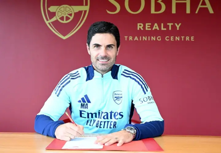 Mikel Arteta, trener Arsenalu, podpisuje dokumenty. Uśmiecha się do aparatu, ubrany w klubowy dres.