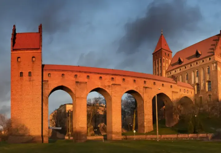 Imponujące zamki na Pomorzu, z cegły i czerwonym dachem, oświetlone zachodzącym słońcem, na tle burzowego nieba.
