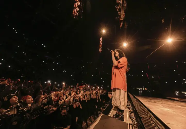 Billie Eilish w Polsce śpiewa dla tłumu fanów, którzy oświetlają scenę telefonami.