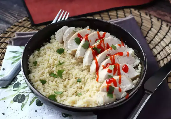Delizioso pollo in padella a fette, servito su un letto di couscous e guarnito con prezzemolo e salsa piccante.