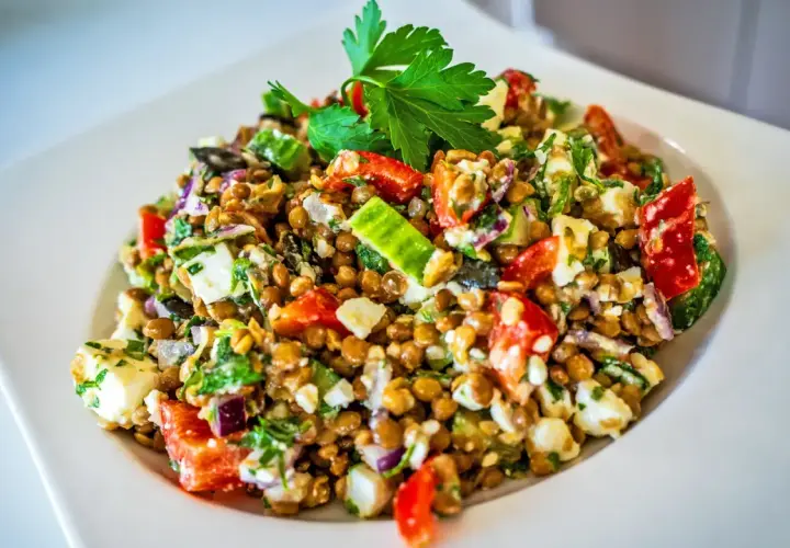 Ein bunter Linsensalat mit Feta, Tomaten, Gurken und frischer Petersilie, garniert mit einem Petersilienblatt.