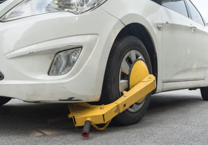 Ruota anteriore di un'auto bianca bloccata da un dispositivo giallo, segno di confisca veicolo.