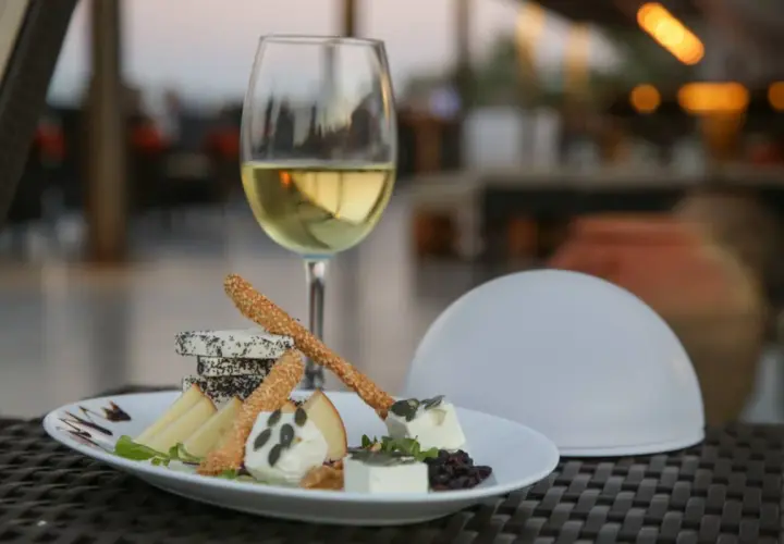 Un verre de vin blanc et une assiette de fromages variés, parfaits pour savoir que manger avec un gewurztraminer.