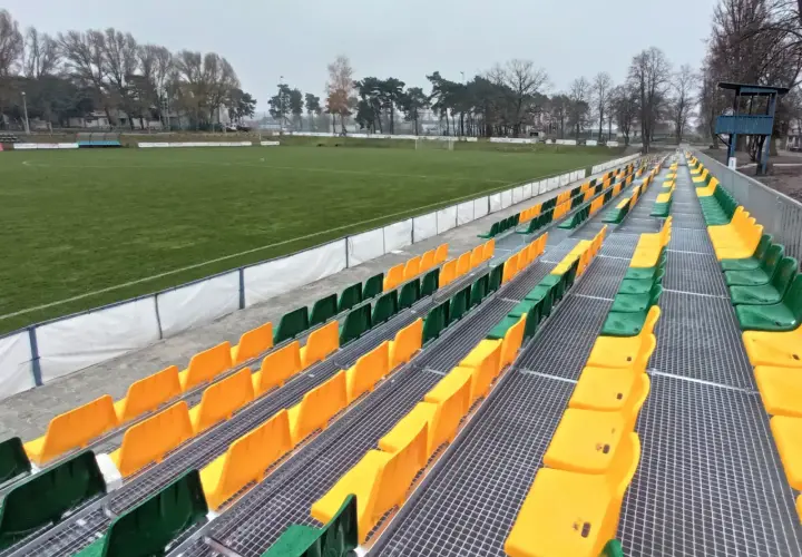 Puste trybuny stadionu Lechii Zielona Góra, z rzędami zielonych i żółtych krzesełek, czekają na kibiców.