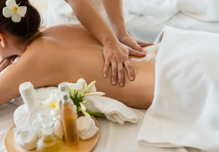 Mains expertes prodiguant un massage américain relaxant sur le dos huilé d'une femme, avec des fleurs de frangipanier et des huiles de massage à proximité.