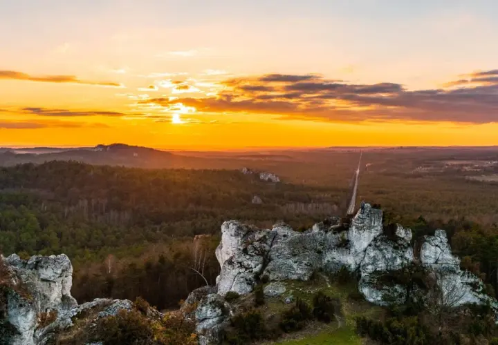 Zachód słońca nad Jurą Krakowsko-Częstochowską. Skaliste formacje i lasy tworzą malownicze krajobrazy, idealne na odkrywanie atrakcji.