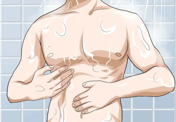 Hombre en la ducha, con agua cayendo sobre su torso. Se toca el pecho, preparándose para depilarse el pecho.