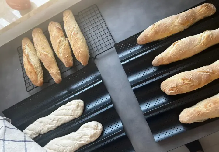 Gotowe do pieczenia bagietki po francusku, świeżo wyrośnięte ciasto i wypieczone bochenki na ruszcie.