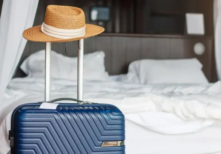 Błękitna walizka i słomkowy kapelusz gotowe do wyjazdu. Zastanawiasz się, co można zabrać z hotelu? Pamiętaj o swoich rzeczach!