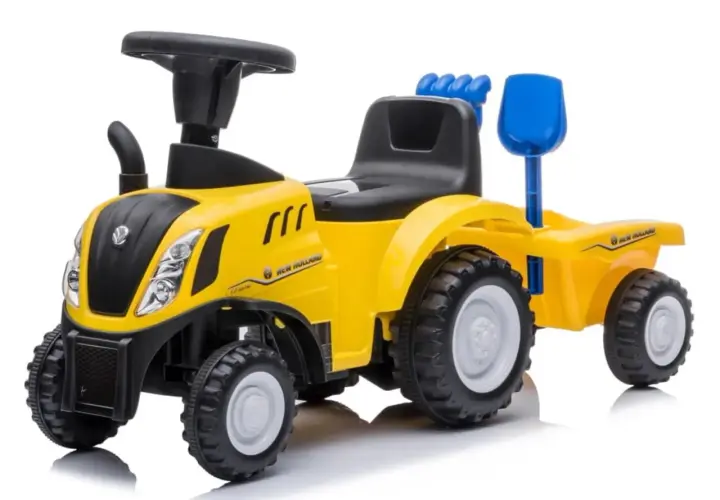 Żółty traktor New Holland z przyczepą, zabawka dla małego rolnika. Ma czarne siedzenie, kierownicę i niebieską łopatkę.
