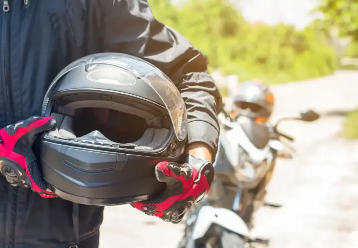 Motocyklista w czerwono-czarnych rękawicach trzyma kask. Warto wiedzieć, co to jest pinlock w kasku, by uniknąć parowania wizjera podczas jazdy.
