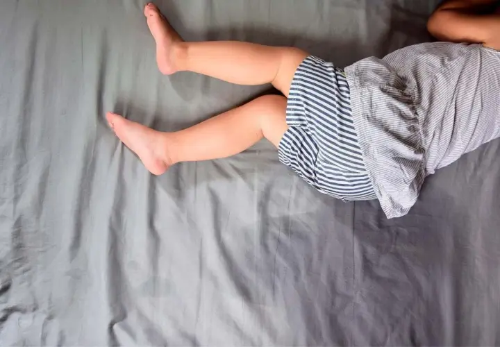 Gambe di bambino su lenzuola grigie. Un piccolo incidente notturno, forse legato all'enuresi notturna, ha lasciato un segno.