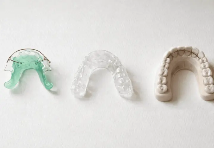 Tres dispositivos dentales: un retenedor verde, un retenedor transparente y un modelo de dientes con barra retenedora.