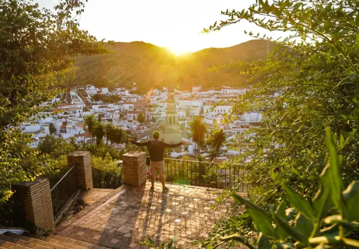 Hombre con brazos abiertos contempla un pueblo blanco en la sierra de Sevilla al atardecer.