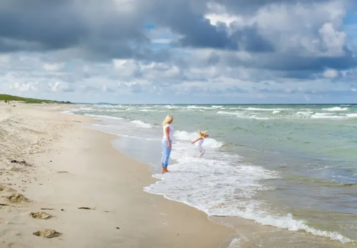 Matka patrzy, jak dziecko bawi się w falach. Czy Szwecja ma dostęp do Morza Północnego? Tak, przez cieśniny Skagerrak i Kattegat.