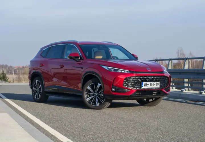 Czerwony MG HS Hybrid na drodze, z widocznym grillem i światłami LED. Elegancki SUV gotowy na podróż.