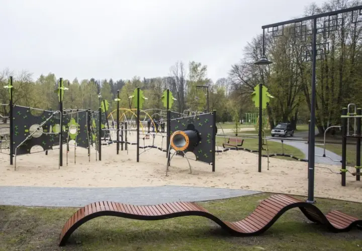 Nowoczesny plac zabaw w parku na zdrowiu z piaskownicą, ściankami wspinaczkowymi i nietypową ławką.