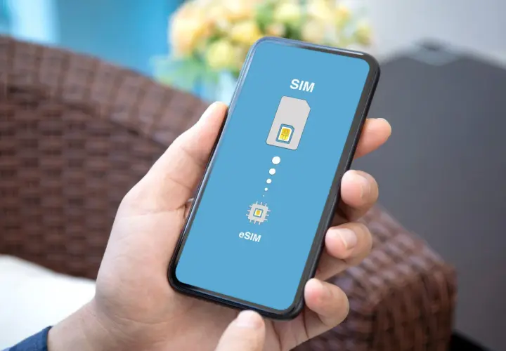 Dłoń trzyma smartfon z ekranem pokazującym ikonę karty SIM i chip eSIM, symbolizując przejście na technologię eSIM.