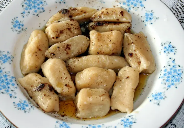 Gotowe pierogi leniwe, polane masłem i posypane cynamonem, czekają na talerzu z niebieskimi kwiatuszkami.