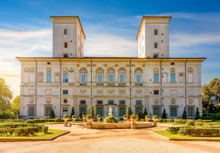 La Villa Borghese à Rome, avec ses tours jumelles et son jardin à la française, sous un ciel bleu éclatant.