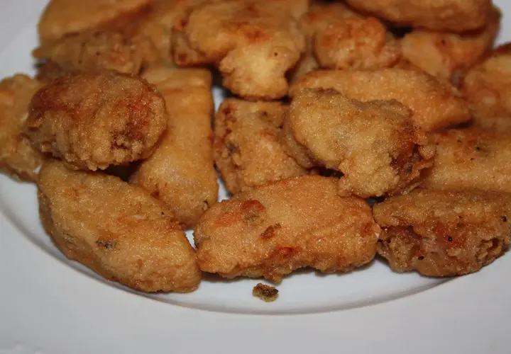 Un plato blanco lleno de trozos dorados y crujientes de japuta en adobo, listos para disfrutar.