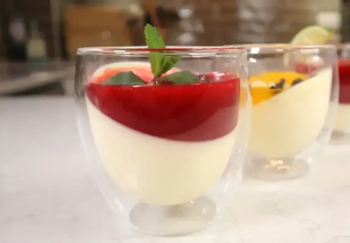 Panna cotta w szklankach z musem malinowym i miętą. Obok deser z musem mango.