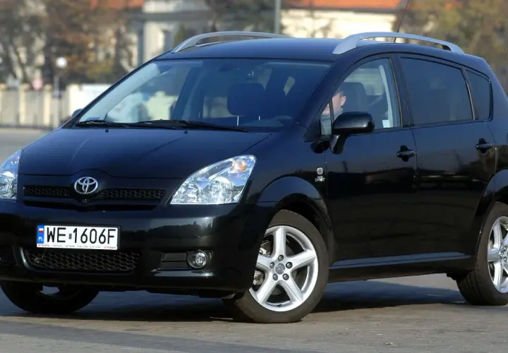 Czarny Toyota Corolla Verso z relingami dachowymi, zaparkowany na ulicy.