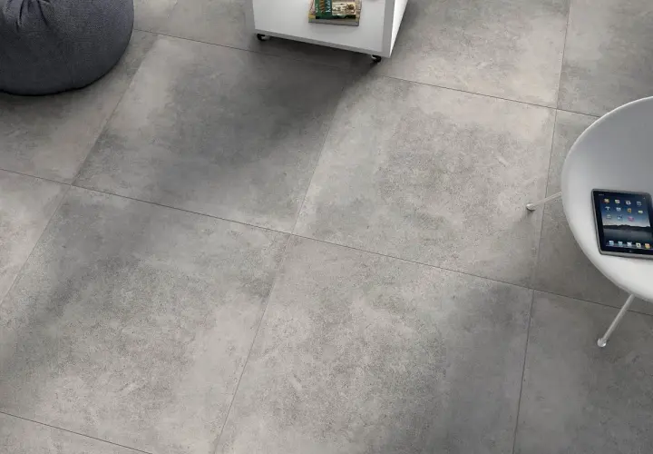 Szare, rektyfikowane płytki tworzą nowoczesną podłogę. Obok wygodny fotel i stolik z książkami.