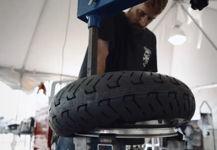 Mecánico revisa un neumático de moto con inscripción 100/90 r18 equivalencia.