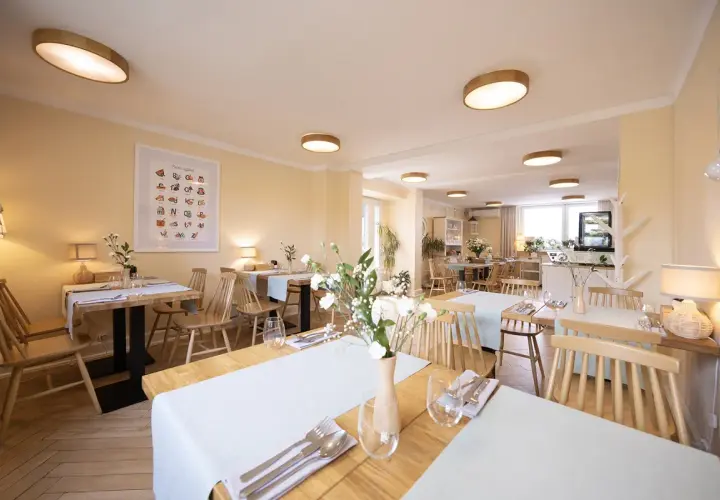 Przytulna restauracja z drewnianymi stołami i krzesłami, idealna na urodziny w łodzi dla dorosłych. Jasne ściany, subtelne oświetlenie i świeże kwiaty tworzą miłą atmosferę.