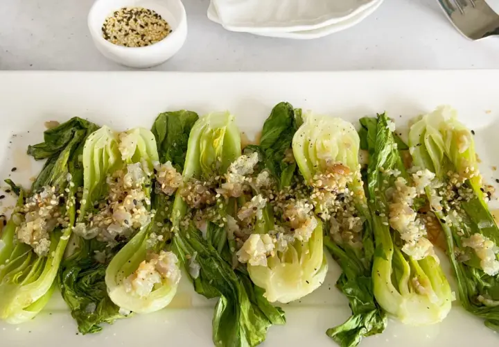 Bok choy tierno salteado con ajo y semillas de sésamo, servido en un plato blanco.