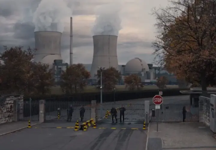 Mroczna elektrownia z chmurami pary nad chłodniami. Strażnicy przy bramie, nie wiadomo, kto jest kim.