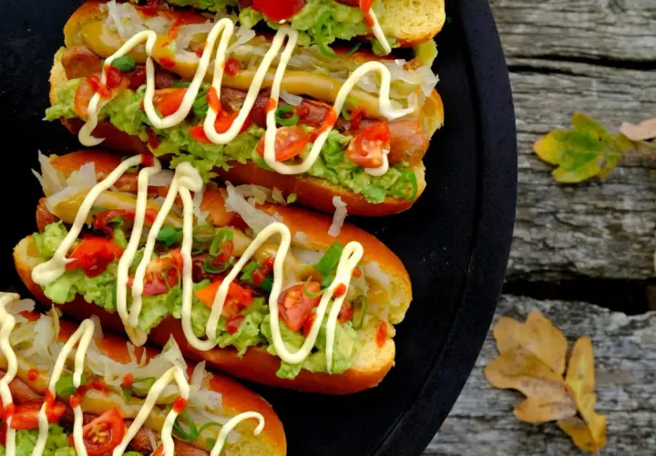 Fyra läckra completos chilenos med avokado, tomat och majonnäs på ett svart fat, redo att avnjutas utomhus bland höstlöven.