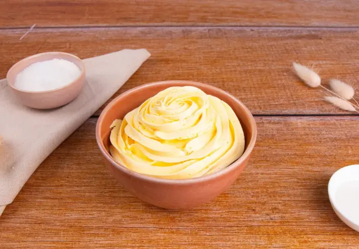 Una ciotola piena di soffice crema al burro, pronta per decorare torte. Accanto, ciotoline con zucchero e decorazioni naturali.