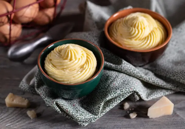 Due ciotole con crema pasticcera salata, guarnita a spirale. In sottofondo uova e formaggio.