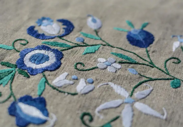Un fichier broderie aux motifs floraux bleus et blancs sur fond beige. Les détails des points de couture sont visibles.