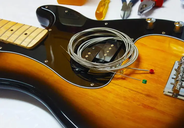 Nowe gitara struny po kolei czekają na założenie. W tle narzędzia do naprawy.