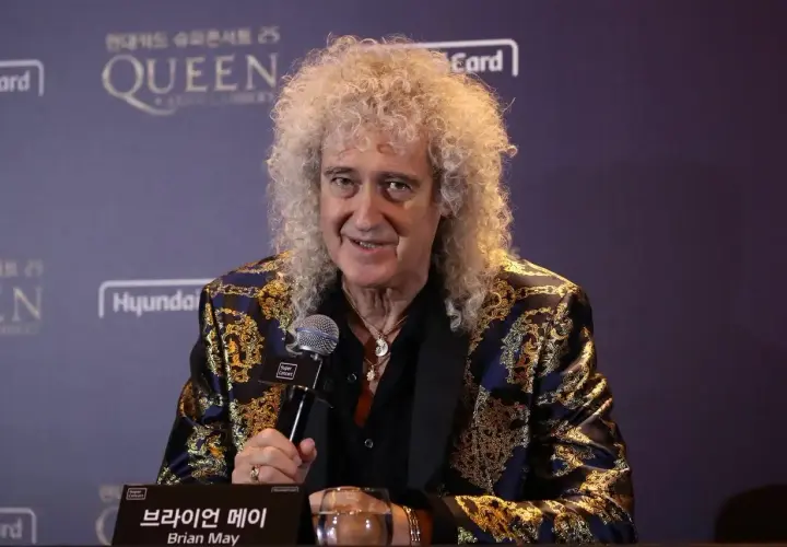 Brian May z zespołu Queen, w ozdobnej marynarce, udziela wywiadu.